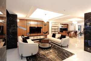 Una sala de estar moderna con un televisor de pantalla plana, dos sofás blancos, una mesa de centro y un piso de mármol.
