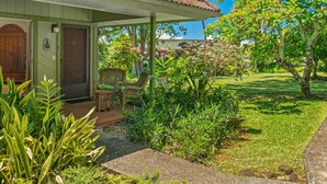Ein Haus mit einer überdachten Veranda, einer Holztür und einem kleinen Garten mit Pflanzen und einer Bank.