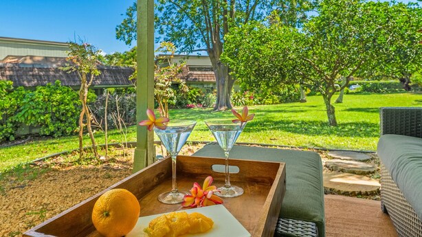 Ein Holztablett mit einer ganzen Orange, einer halben Orange und zwei Martini-Gläsern mit Blumen auf einer Terrasse.