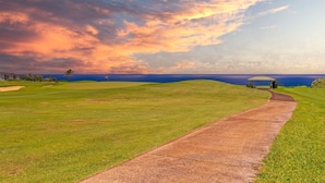 Ein Golfplatz mit einem klaren Weg zu einem Pavillon, umgeben von üppigem Grün und Blick auf das Meer.