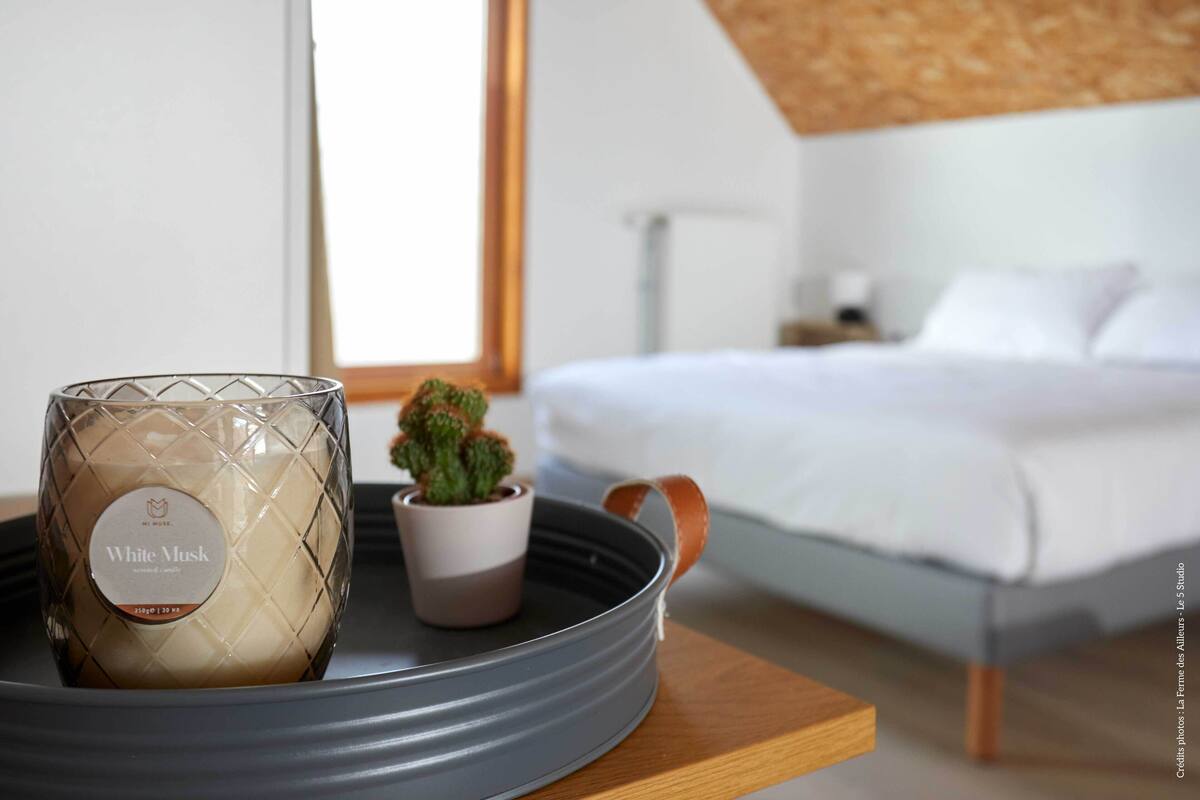 Quarto com cama, mesa de cabeceira com uma vela e uma pequena planta em vaso.