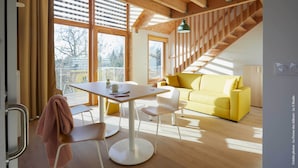 Ein modernes Interieur mit einer Holztreppe, einem gelben Sofa und einer Essecke mit Tisch und Stühlen.