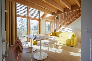 Un interior moderno con una escalera de madera, un sofá amarillo y un comedor con mesa y sillas.
