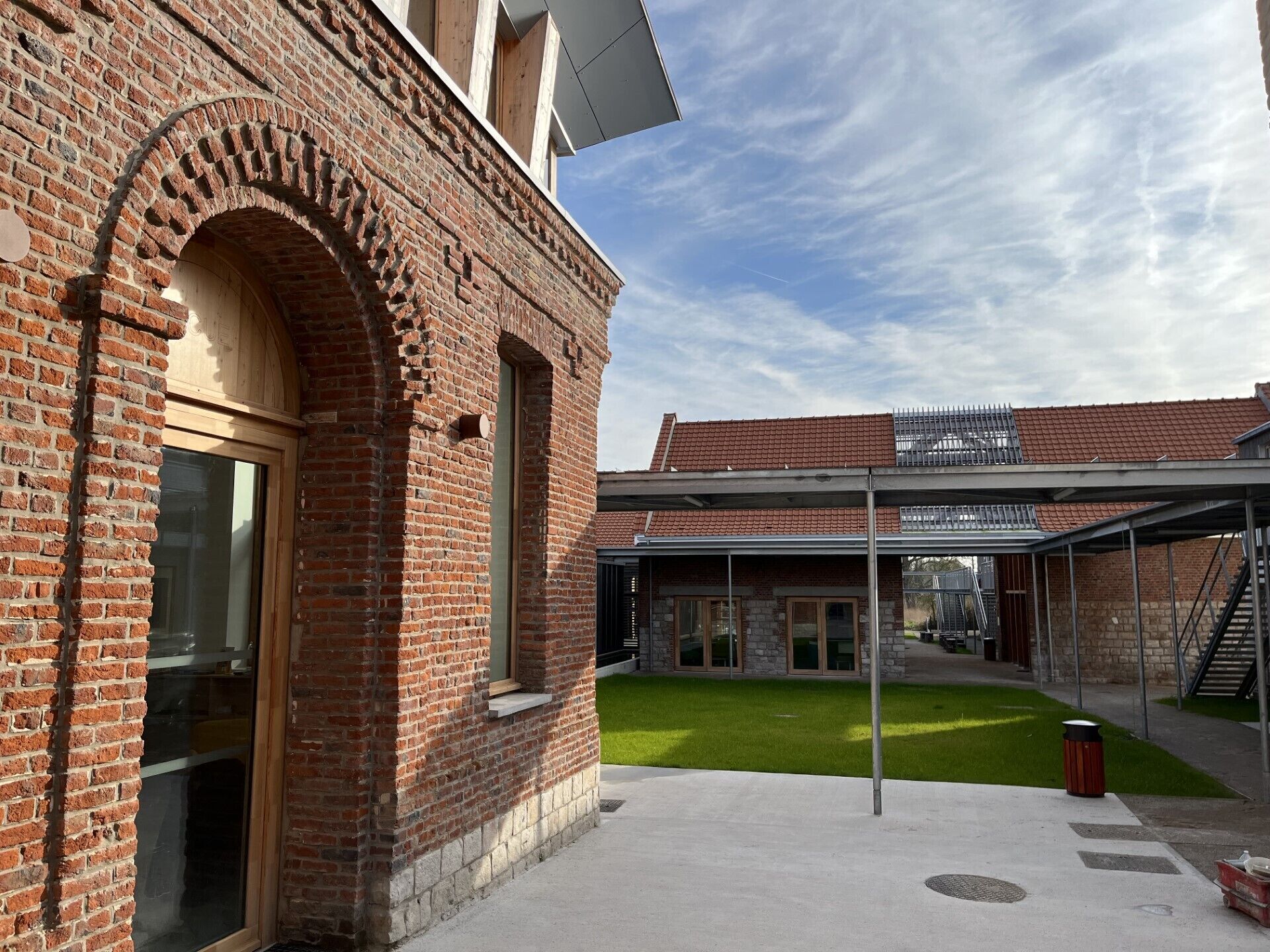 A courtyard with a brick building, a covered walkway, and a grassy area.