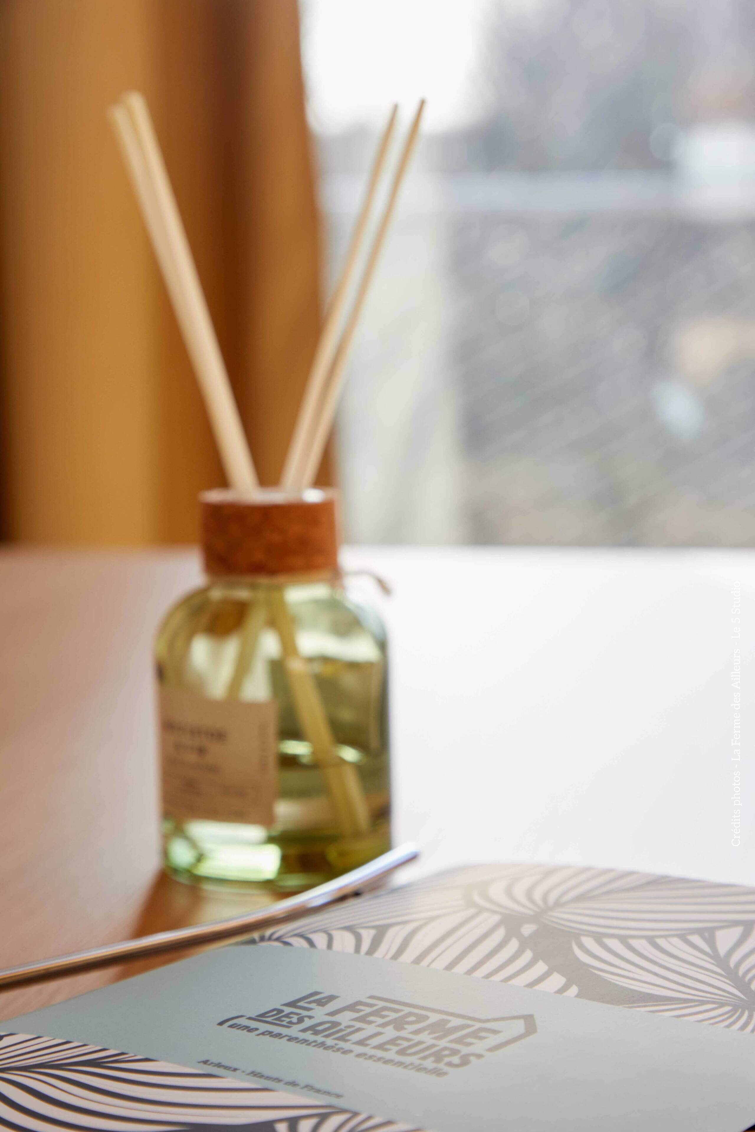 Un difusor de cañas en botella con tapón de corcho y palitos aromáticos sobre una mesa.