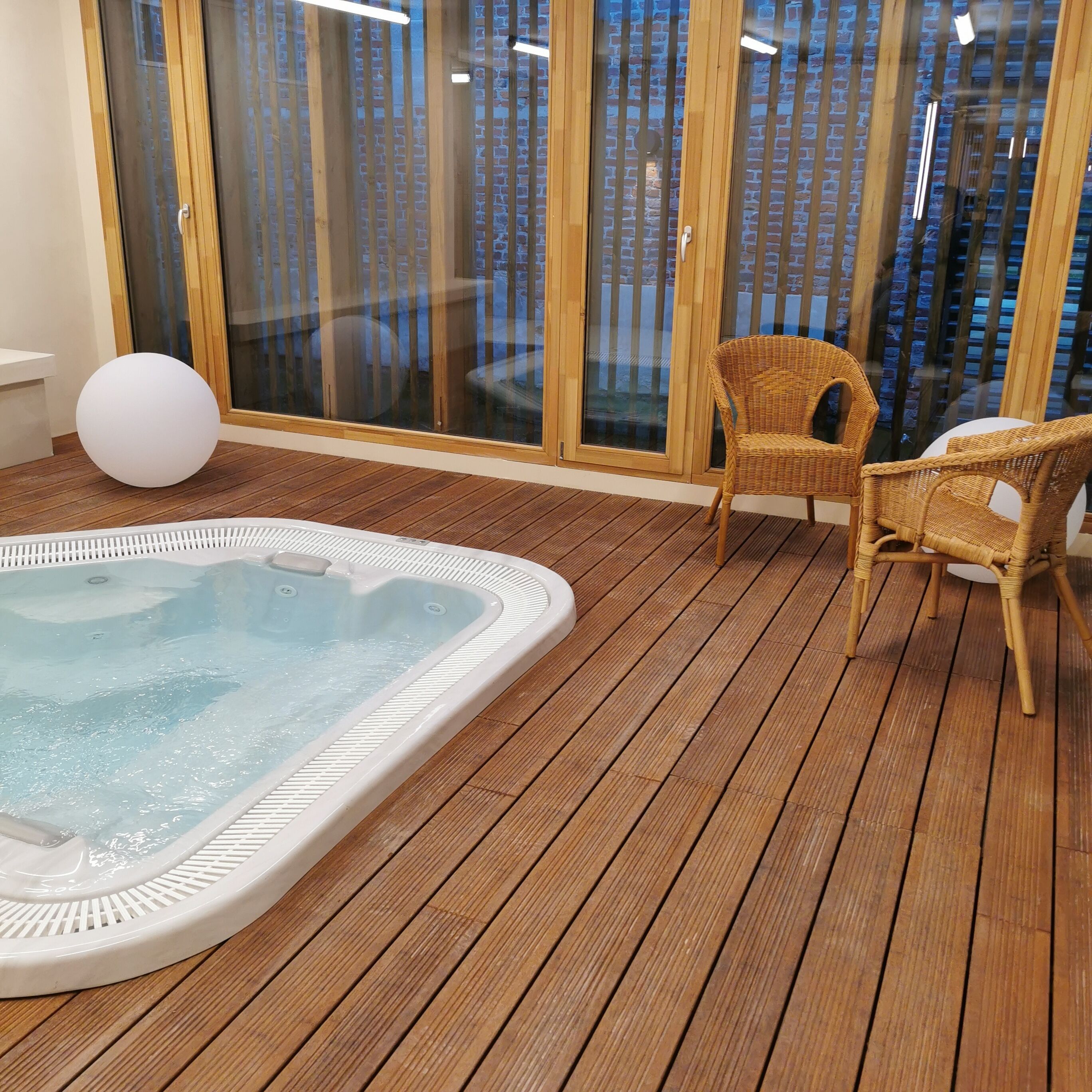 Une terrasse en bois avec un jacuzzi et des fauteuils en osier.