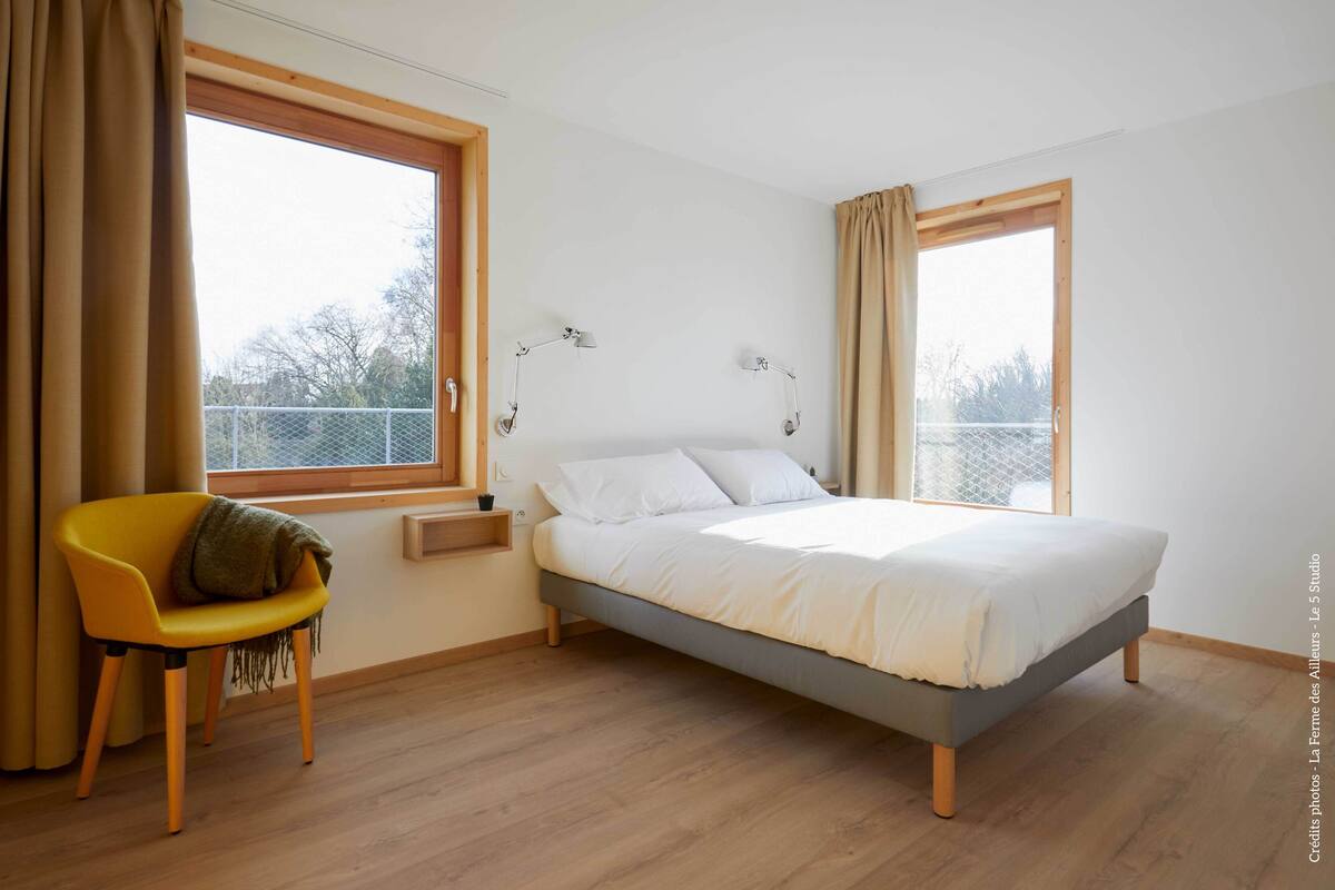 Quarto com uma cama, uma cadeira, duas luminárias de cabeceira e uma janela com cortinas.