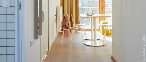A modern interior with a wooden floor, a dining area with a table and chairs, and a large window providing natural light.
