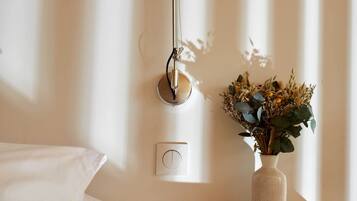 Ein ordentlich eingerichtetes Schlafzimmer mit Nachttischlampe, einer Vase mit Trockenblumen und einer Steckdose an der Wand.