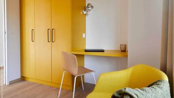 Una habitación con un armario amarillo, una silla de madera, un sofá amarillo y una mesita con una lámpara.