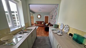Een keuken met een groot raam, een spoelbak, een houten aanrecht en een zithoek met een bank en een tafel.