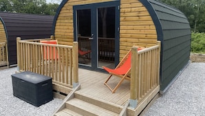 Une cabane en bois avec un toit incurvé, une porte en verre et une petite terrasse avec une chaise.
