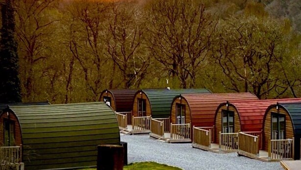 A row of cabins with arched doorways and wooden railings, set in a wooded area. - Forest Pod 4 (Pet Friendly) -  a glamping pod that sleeps 2 guests  in 1 bedroom (Neath)