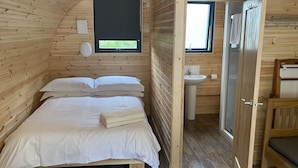 A wooden cabin room with a bed, a window, a sink, and a door.