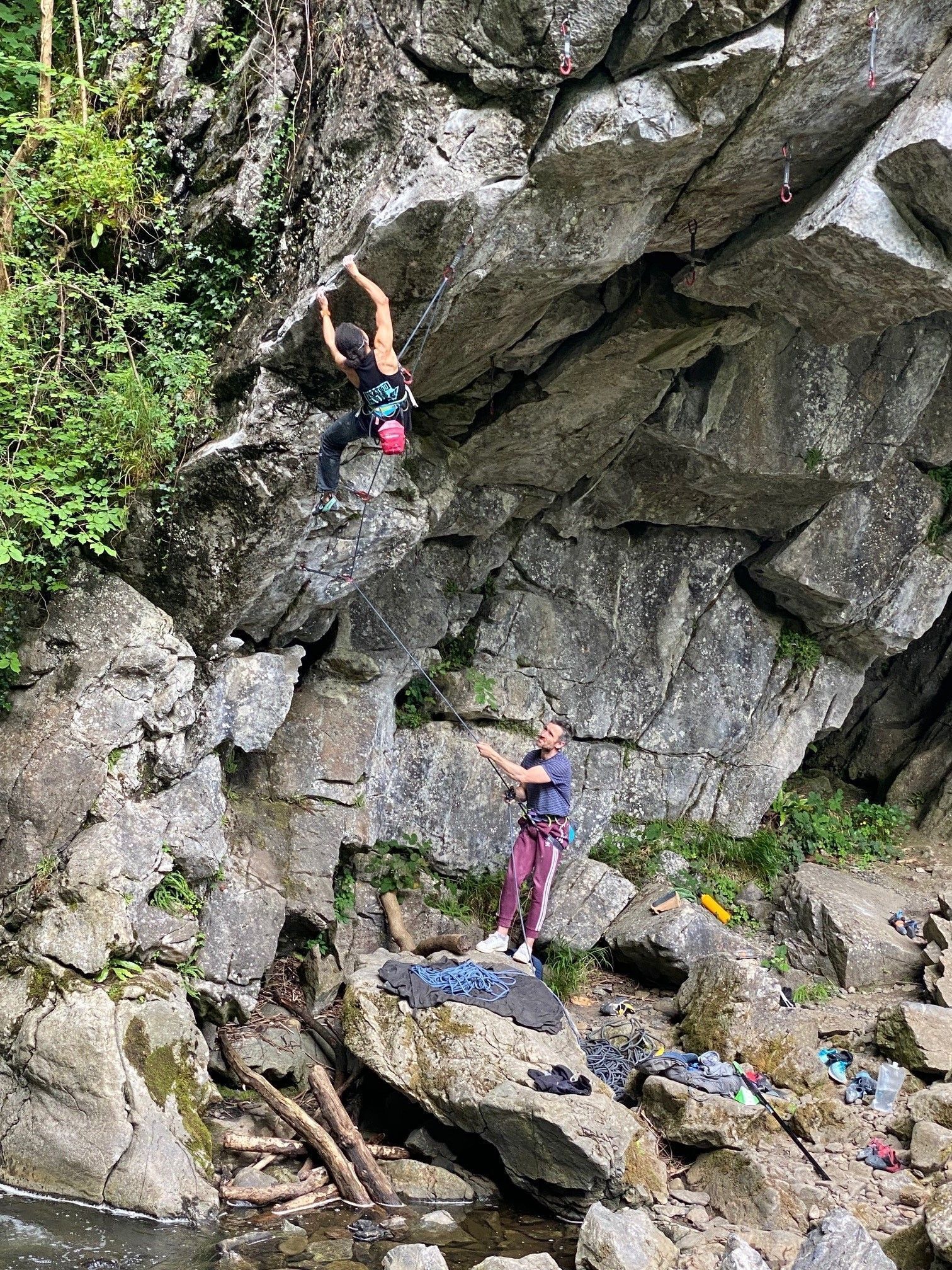 A person climbing a rocky cliff with another person assisting.