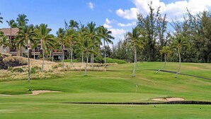 A golf course with a clubhouse, palm trees, and a clear sky.