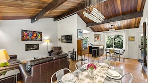 A spacious living area with a wooden ceiling, a dining table set for six, and a comfortable leather sofa. - Moondance - Contemporary Riverfront Home (Monte Rio)