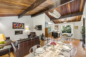Amplia sala de estar con techo de madera, una mesa de comedor preparada para seis personas y un cómodo sofá de cuero.