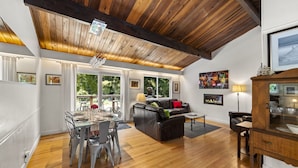 A spacious living area with a wooden ceiling, a dining table set for four, a leather sofa, and a fireplace. - Moondance - Contemporary Riverfront Home (Monte Rio)
