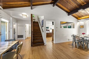 A spacious room with wooden floors, a dining area with a table set for four, and a staircase leading to another level. - Moondance - Contemporary Riverfront Home (Monte Rio)