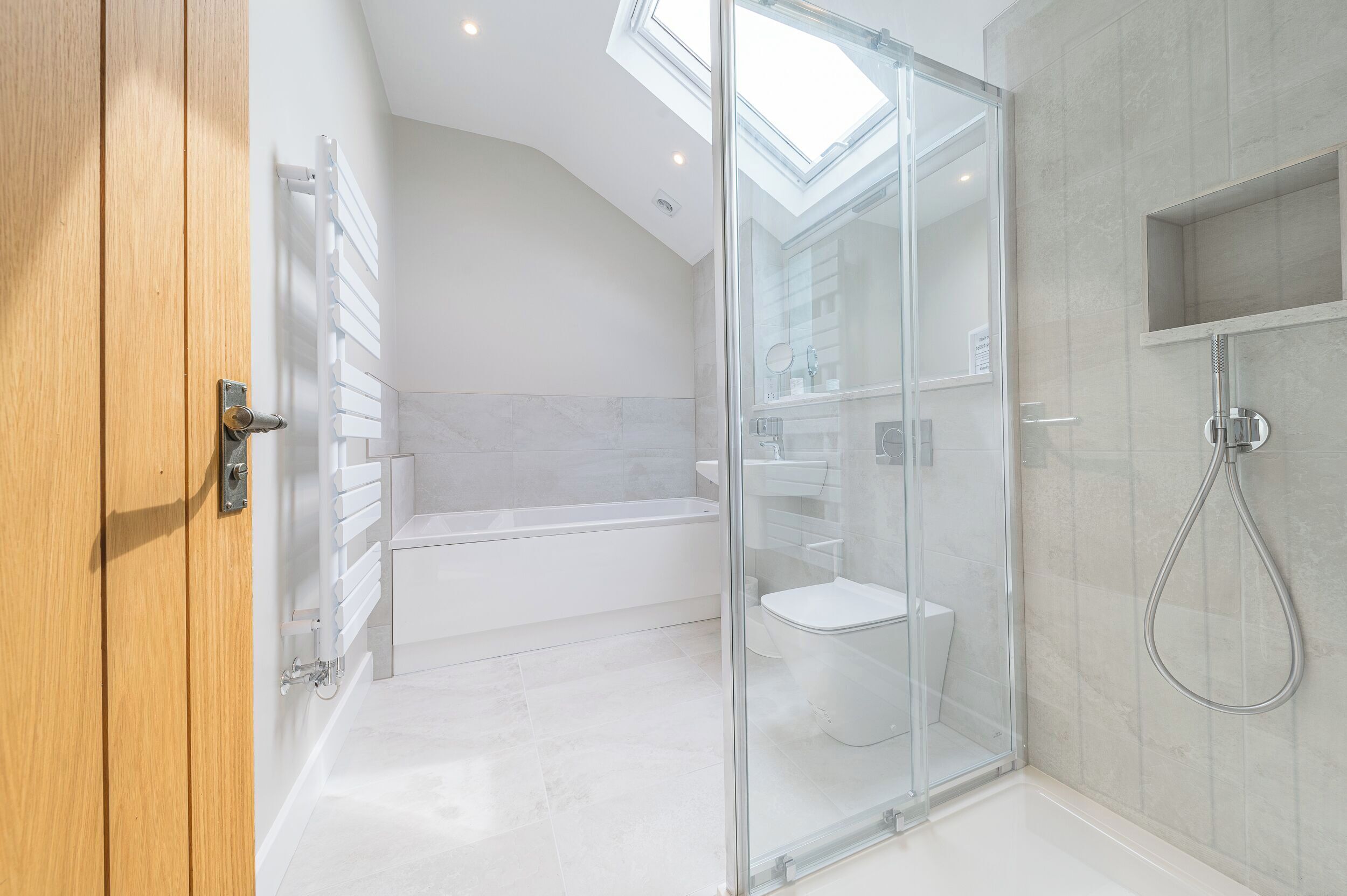 A modern bathroom with a glass shower enclosure, a freestanding bathtub, and a skylight above.