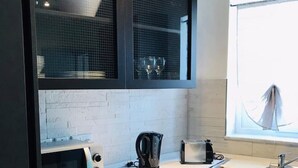 A modern kitchen with a built-in microwave, toaster, kettle, and a window with a view of a sailboat. - Lovely studio apart in Msida (L-MSIDA)