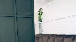 A neatly made bed with a patterned bedspread, a bedside lamp, and a wall-mounted shelf with a plant. - Lovely studio apart in Msida (L-MSIDA)