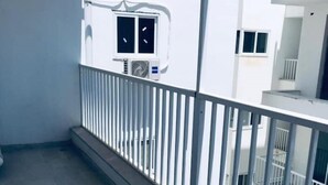 A balcony with a white railing, a tiled floor, and a view of a white building with multiple windows and balconies. - Lovely studio apart in Msida (L-MSIDA)
