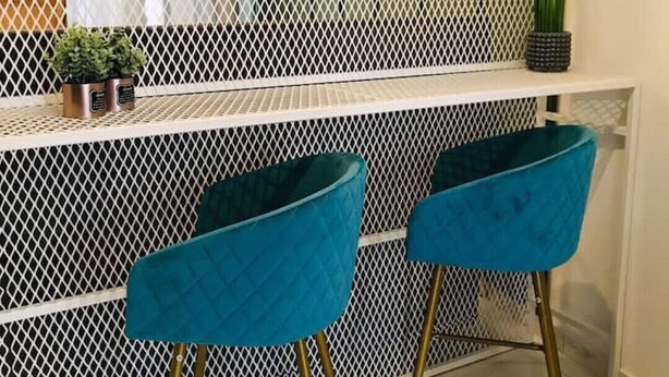 A modern bar area with a white mesh partition, two teal bar stools, and a potted plant on a shelf. - Lovely studio apart in Msida (L-MSIDA)