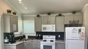 Una cocina con armarios blancos, un refrigerador blanco, una estufa blanca, un microondas y un fregadero.