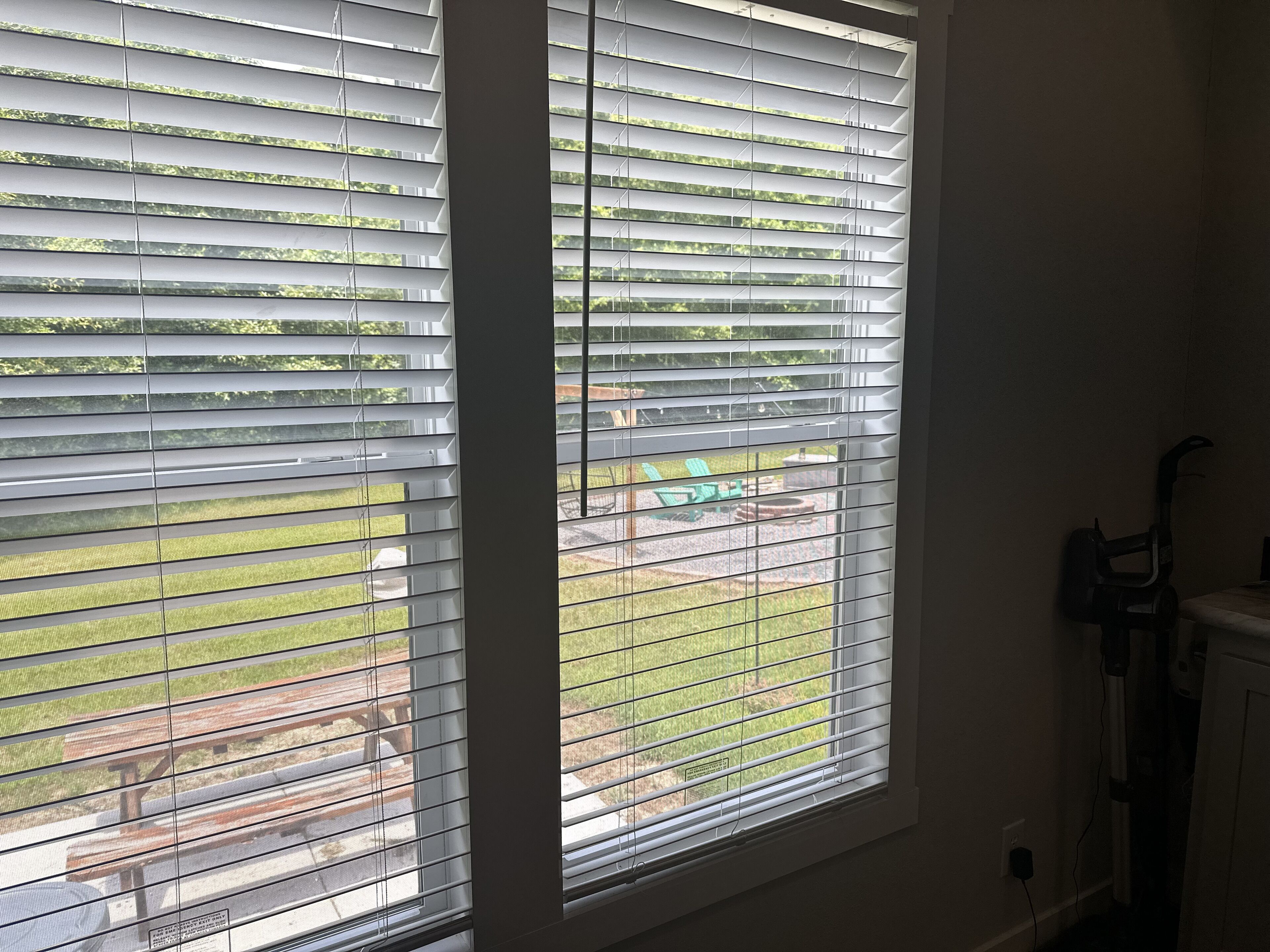 Ein Fenster mit horizontalen Jalousien, Blick auf eine Terrasse mit Gartenmöbeln und ein Heizkörper an der Wand.