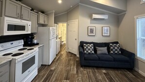 Una cocina compacta con electrodomésticos blancos, un sofá de color oscuro y piso de madera.