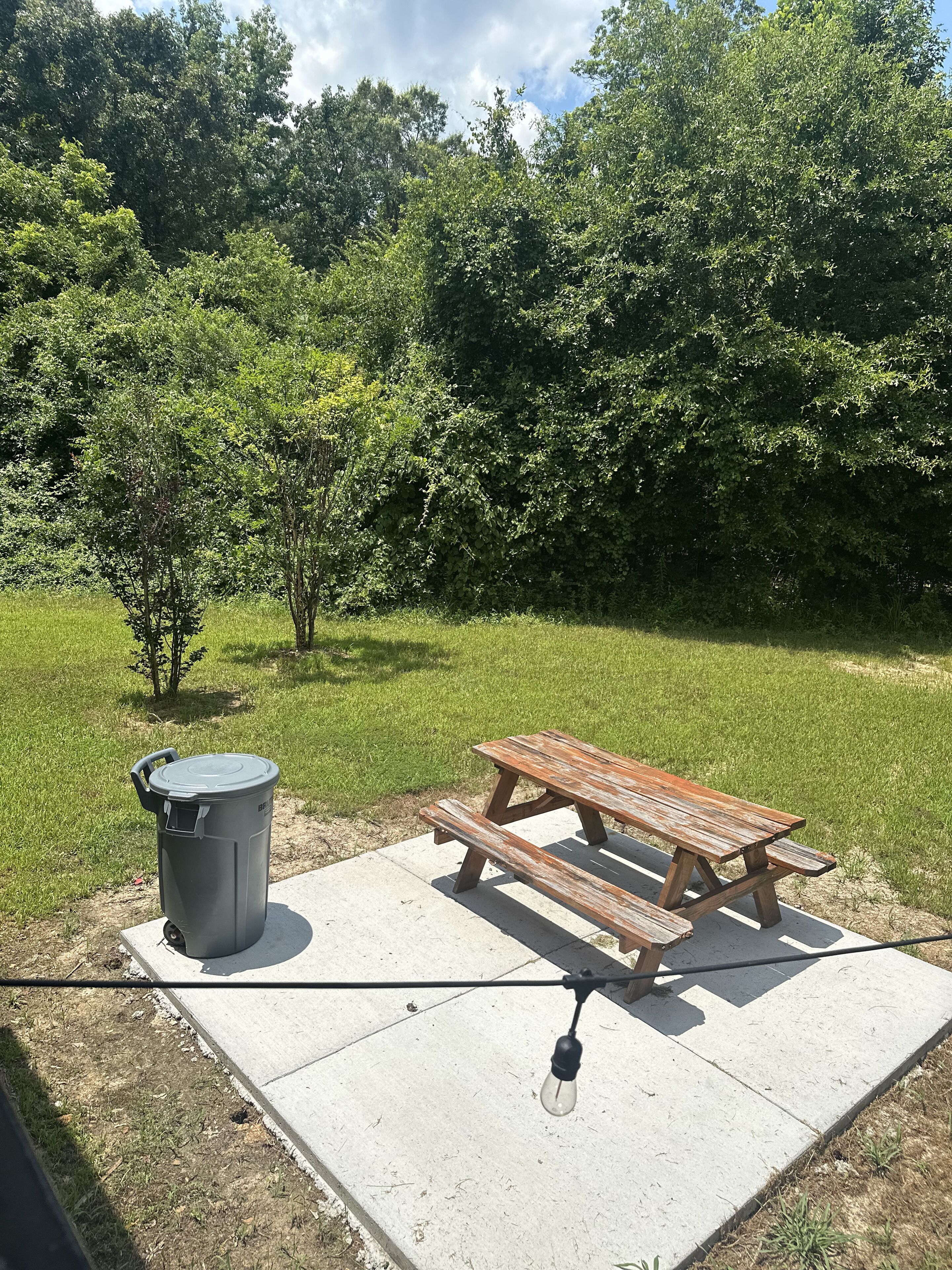 A picnic table with a trash can and a light bulb on a concrete surface.