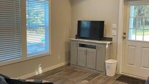 Una sala de estar con televisión sobre un mueble, una puerta y una ventana con persianas.
