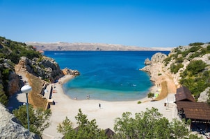 Escena de playa costera con aguas azules cristalinas, terreno rocoso y algunas personas disfrutando.