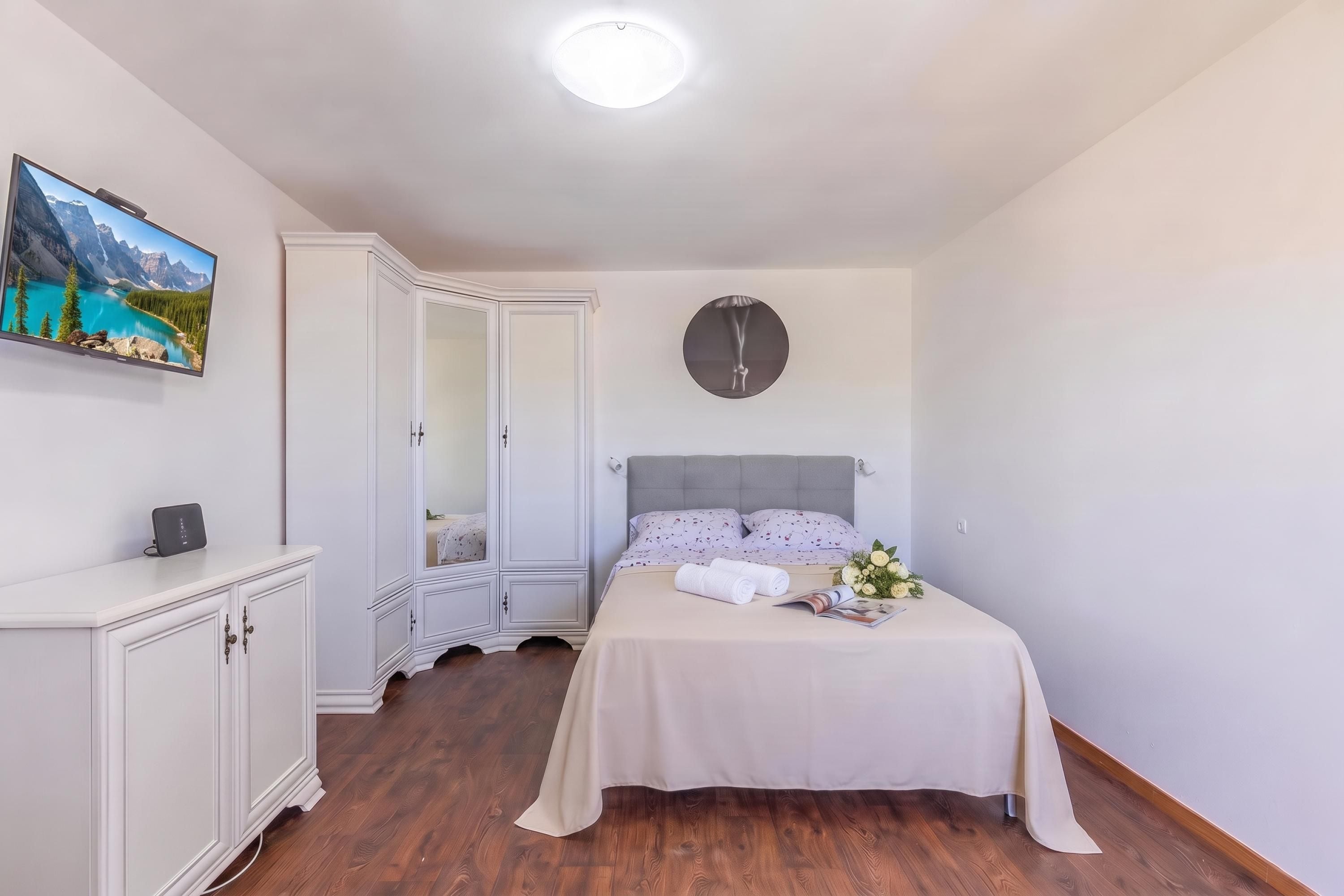 Um quarto com cama, guarda-roupa, mesa de cabeceira, relógio na parede e um quadro na parede.