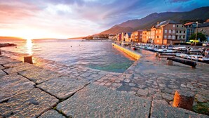 A waterfront promenade with cobblestone pavement, boats docked along the shore, and buildings with balconies overlooking the water. - 1BR Seafront Apartment Sanja Karlobag (Karlobag)