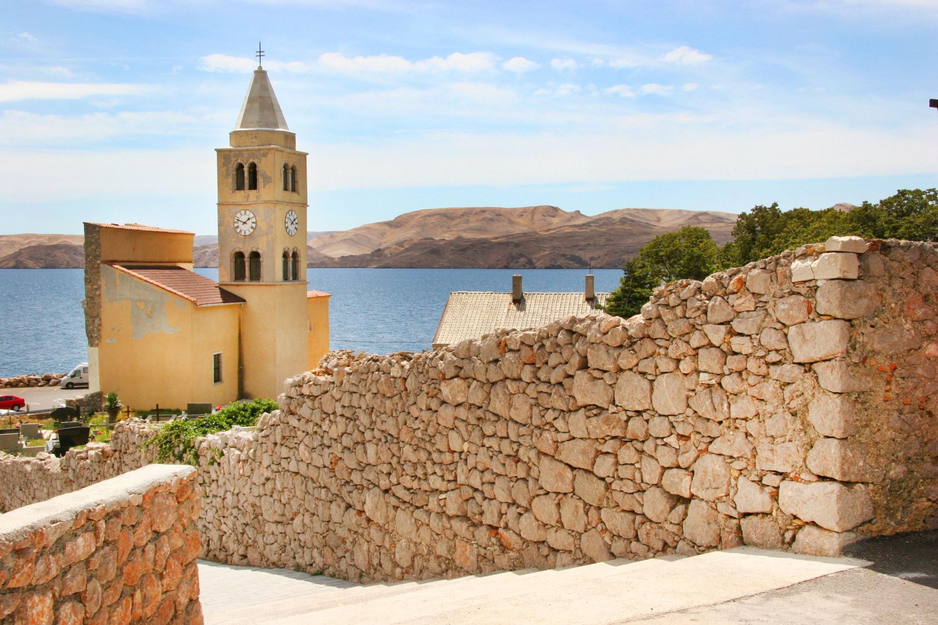 Une ville côtière dotée d’un clocher d’église imposant, de murs en pierre et offrant une vue sur la mer.