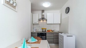 A compact kitchen with white cabinets, a built-in stove, a dishwasher, and a small refrigerator. - 1BR Seafront Apartment Sanja Karlobag (Karlobag)