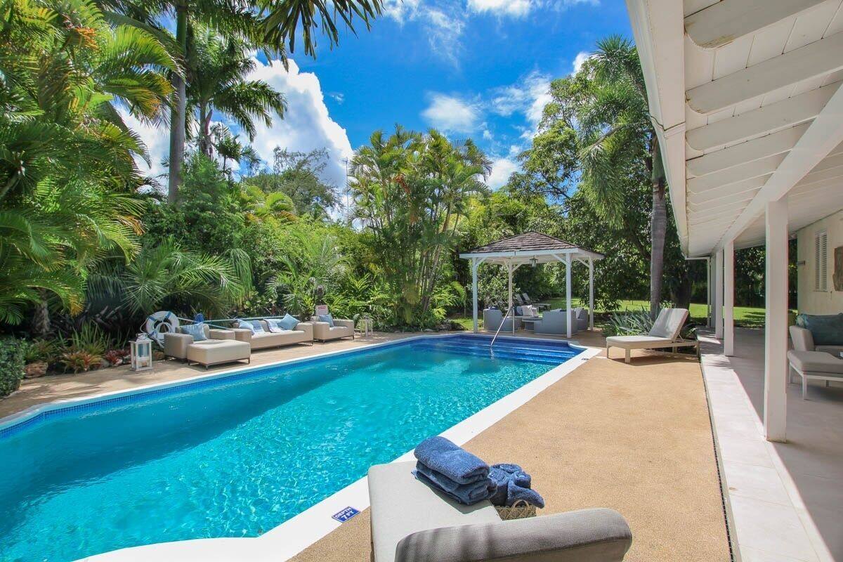 Piscina com espreguiçadeiras, um gazebo e vegetação exuberante.