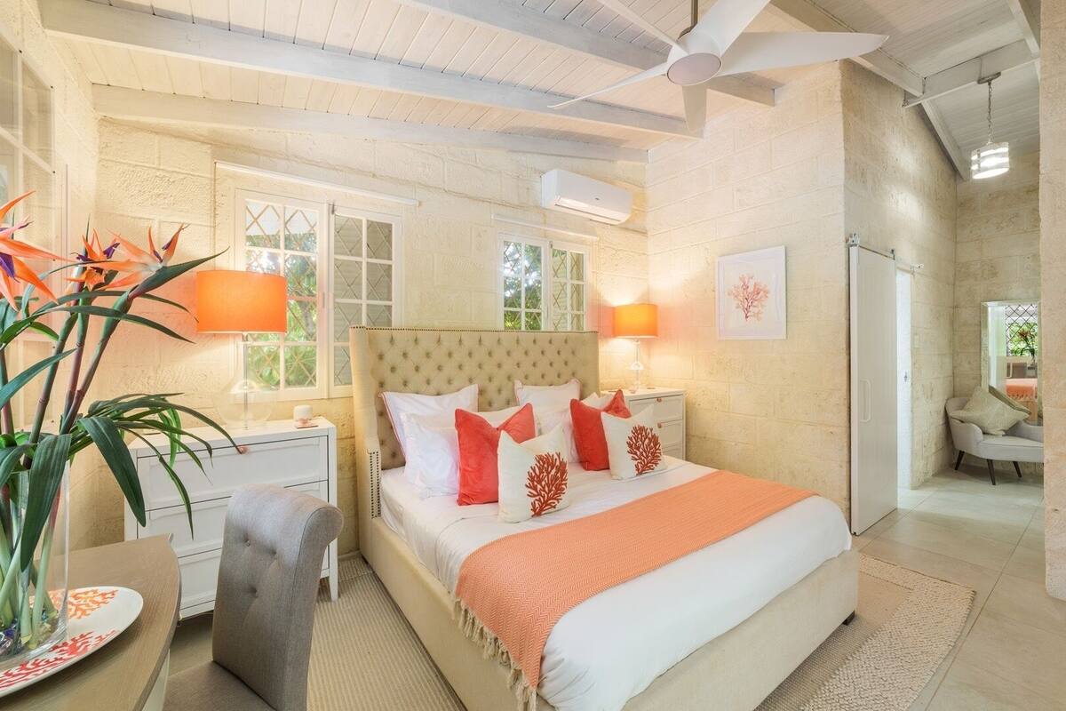 Quarto com cama, mesas de cabeceira, uma cadeira, uma planta em vaso e uma janela.