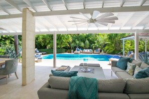 An outdoor pool area with a covered seating area, lounge chairs, and a ceiling fan. - Palm Grove by Bluescape (Mullins)