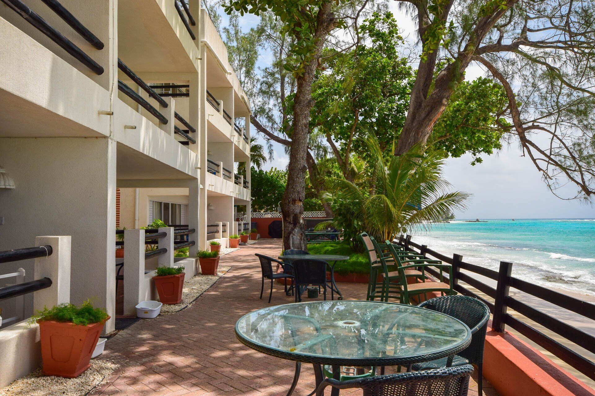 A balcony with a glass table and chairs overlooking a beach.