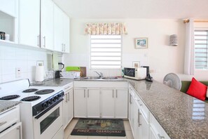 A kitchen with white cabinets, a stove, a microwave, and a sink. - 3 Sea Star by BSL Rentals (Worthing)