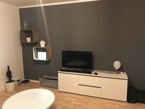 Ein modernes Wohnzimmer mit Flachbildfernseher, einem weißen Schrank, einer kleinen Ablage mit Dekoration und einer weißen Badewanne.