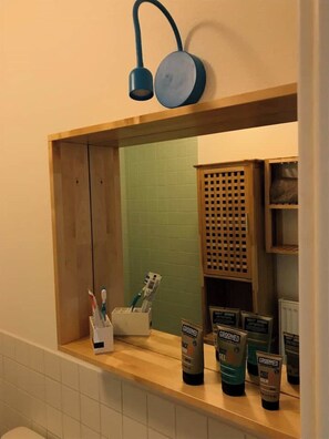 A bathroom with a wooden vanity, a mirror, and toiletries including a toothbrush holder and grooming products.