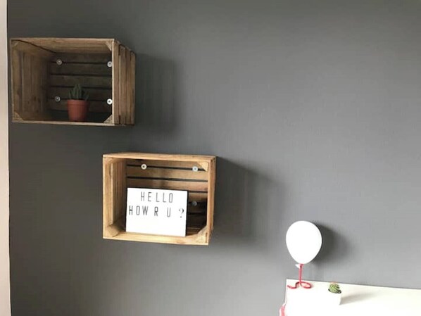 A wall with two wooden crates, one containing a potted plant and the other with a sign that reads "HELLO HOWRU?".