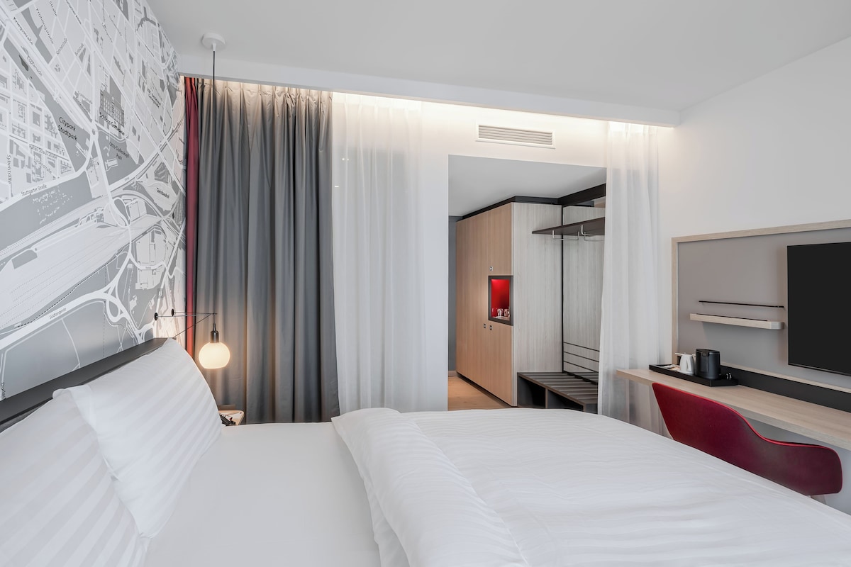 Una habitación de hotel moderna con una cama grande, un escritorio con silla, un televisor y un armario.