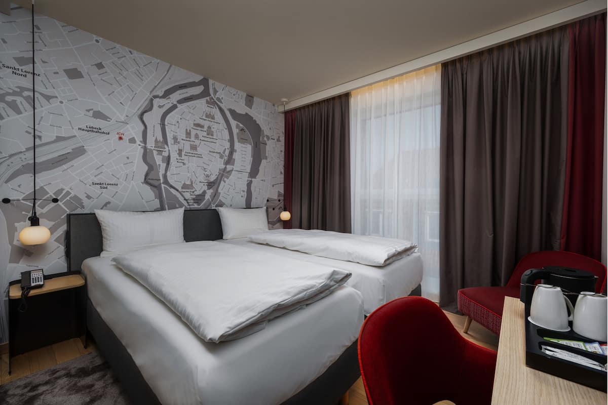 A hotel room with two beds, a map on the wall, a desk with a coffee maker, and a red chair.