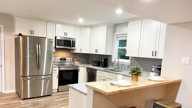 A modern kitchen with white cabinets, stainless steel appliances, a wooden island with stools, and a herringbone-patterned backsplash.
